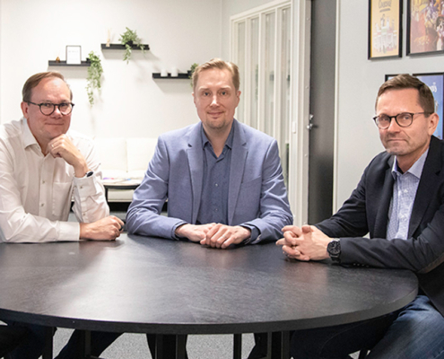 Kuvassa Timo Yli-Salomäki, Nicholas Nordström ja Mika Huovinen istumassa yhdessä pöydän äärellä.