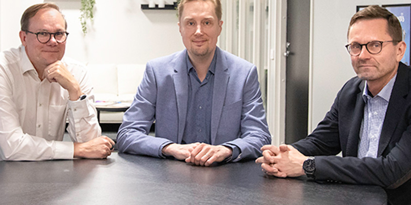Kuvassa Timo Yli-Salomäki, Nicholas Nordström ja Mika Huovinen istumassa yhdessä pöydän äärellä.